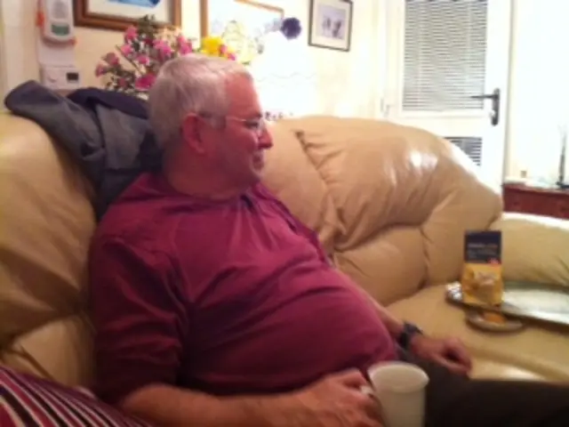 In this image I can see a person sitting on the couch and the person is wearing red shirt, black...