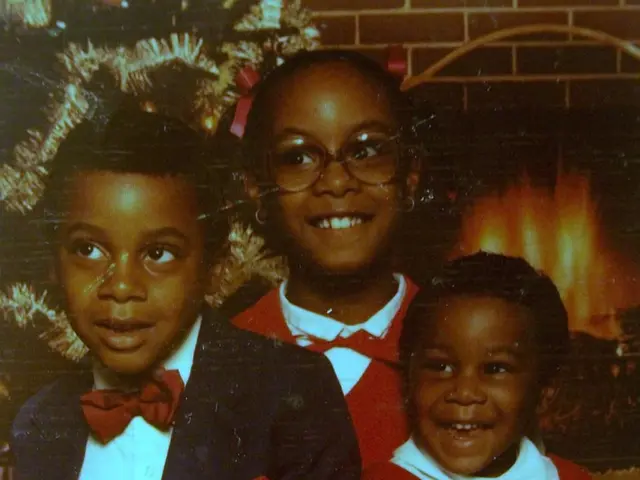 In the image there are three kids laughing, on the back there is a christmas tree followed by...