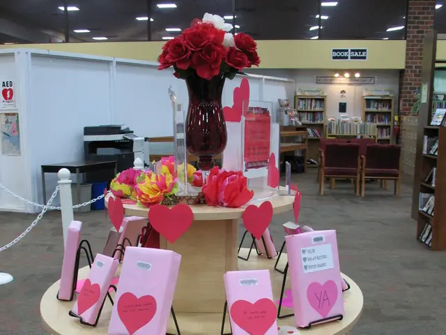 This picture shows a flower vase, flowers and some cards on the table. In the background we can...